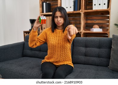 Young Hispanic Woman Playing Colorful Puzzle Cube Intelligence Game Pointing With Finger To The Camera And To You, Confident Gesture Looking Serious 