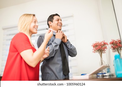 Young Hispanic Woman Putting On Make Up And Man Getting Dressed At Home