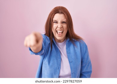 Young hispanic woman with red hair standing over pink background pointing displeased and frustrated to the camera, angry and furious with you  - Shutterstock ID 2297827059