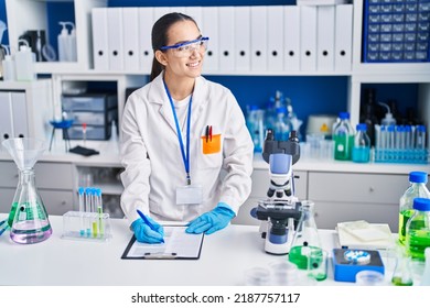 Young Hispanic Woman Scientist Writing On Document Working At Laboratory