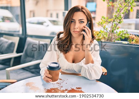Young hispanic woman with serious expression using smartphone sitting at the coffee shop terrace.