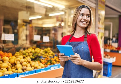 Young hispanic woman shop assistant using touchpad at fruit market - Powered by Shutterstock