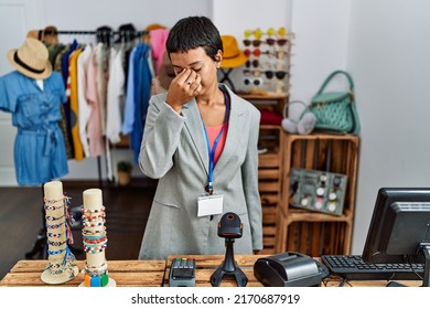 Young hispanic woman with short hair working as manager at retail boutique tired rubbing nose and eyes feeling fatigue and headache. stress and frustration concept. 