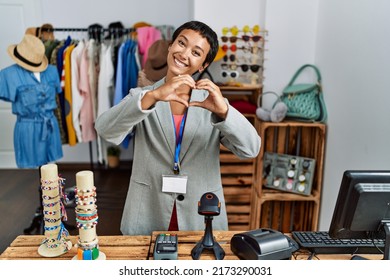 Young Hispanic Woman With Short Hair Working As Manager At Retail Boutique Smiling In Love Doing Heart Symbol Shape With Hands. Romantic Concept. 