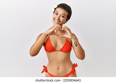 Young Hispanic Woman With Short Hair Wearing Bikini Smiling In Love Doing Heart Symbol Shape With Hands. Romantic Concept. 