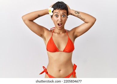 Young Hispanic Woman With Short Hair Wearing Bikini Crazy And Scared With Hands On Head, Afraid And Surprised Of Shock With Open Mouth 