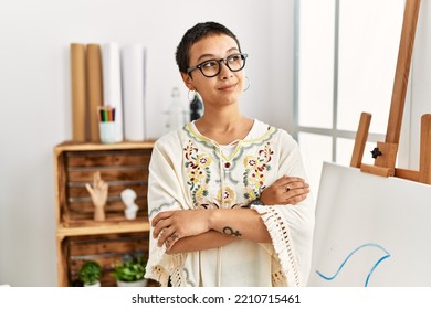 Young Hispanic Woman With Short Hair At Art Studio Smiling Looking To The Side And Staring Away Thinking. 