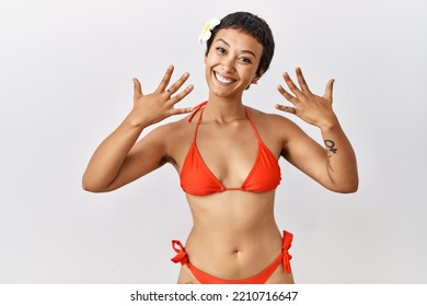 Young Hispanic Woman With Short Hair Wearing Bikini Showing And Pointing Up With Fingers Number Ten While Smiling Confident And Happy. 