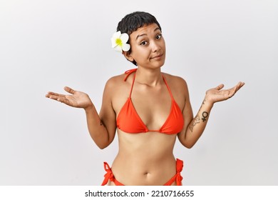 Young Hispanic Woman With Short Hair Wearing Bikini Clueless And Confused Expression With Arms And Hands Raised. Doubt Concept. 