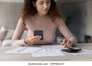 Young Hispanic Woman Sit At Desk Calculate Household Expenses Expenditures On Machine Pay Online On Cellphone. Latin Female Renter Manage Family Budget Finances Using Smartphone. Banking Concept.