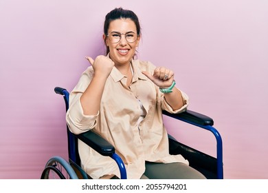 Young hispanic woman sitting on wheelchair pointing to the back behind with hand and thumbs up, smiling confident  - Powered by Shutterstock