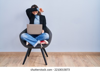 Young Hispanic Woman Sitting On Chair Using Computer Laptop Smiling Cheerful Playing Peek A Boo With Hands Showing Face. Surprised And Exited 