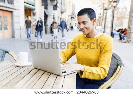 young hispanic woman skinhead using laptop or computer in urban city cafe terrace or coffee shop, Portrait of Latin female with short hair in street outdoors in autumn season