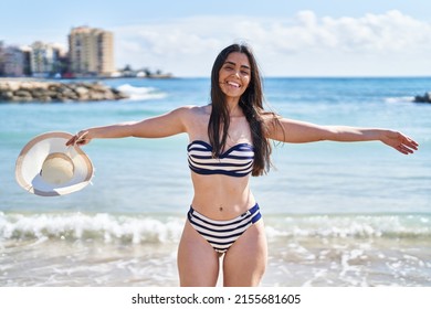 Young hispanic woman smiling confident wearing bikini and holding summer hat at seaside