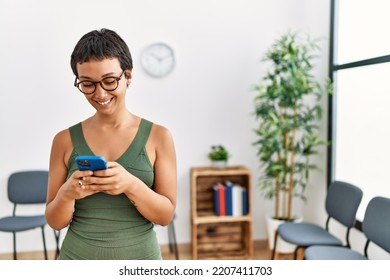 Young hispanic woman smiling confident using smartphone standing at waiting room - Powered by Shutterstock