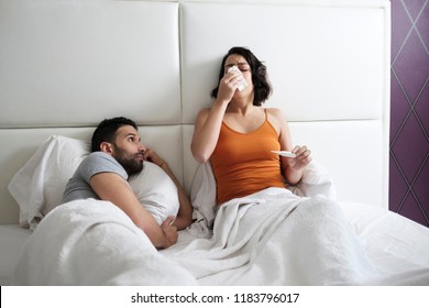 Young Hispanic Woman Sneezing For Allergy At Home. Sick Latina Girl With Cold And Flu, Spreading Disease Germs And Infecting Her Partner Sleeping In The Same Bed