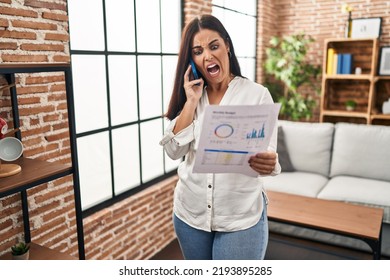 Young hispanic woman speaking on the phone about bills angry and mad screaming frustrated and furious, shouting with anger. rage and aggressive concept.  - Shutterstock ID 2193895285