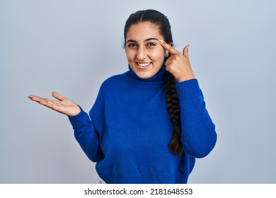 Young hispanic woman standing over isolated background confused and annoyed with open palm showing copy space and pointing finger to forehead. think about it.  - Shutterstock ID 2181648553