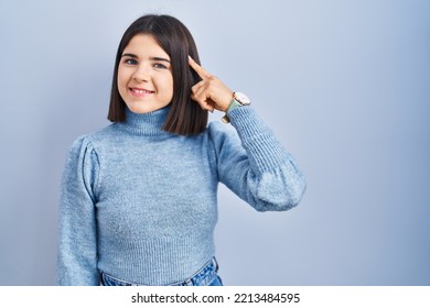 Young Hispanic Woman Standing Over Blue Background Smiling Pointing To Head With One Finger, Great Idea Or Thought, Good Memory 