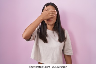 Young Hispanic Woman Standing Over Pink Background Covering Eyes With Hand, Looking Serious And Sad. Sightless, Hiding And Rejection Concept 