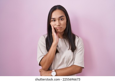 Young hispanic woman standing over pink background thinking looking tired and bored with depression problems with crossed arms. 