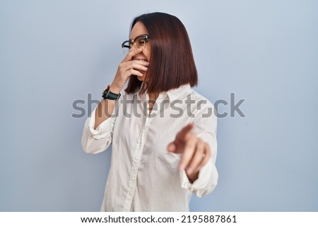 Young hispanic woman standing over white background laughing at you, pointing finger to the camera with hand over body, shame expression 