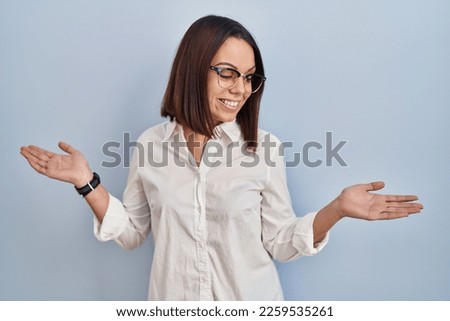 Young hispanic woman standing over white background smiling showing both hands open palms, presenting and advertising comparison and balance 
