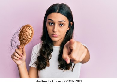 Young Hispanic Woman Styling Hair Using Comb Pointing With Finger To The Camera And To You, Confident Gesture Looking Serious 