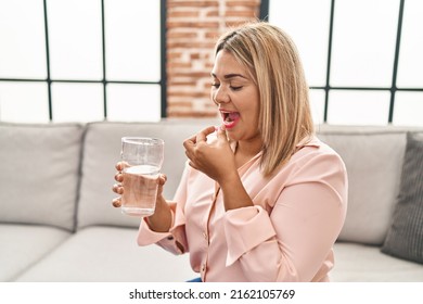 Young Hispanic Woman Taking Pill Sitting On Sofa At Home