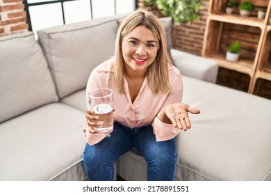 Young Hispanic Woman Taking Pill Sitting On Sofa At Home