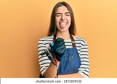 Young Hispanic Woman Tattoo Artist Wearing Professional Uniform And Gloves Sticking Tongue Out Happy With Funny Expression. 