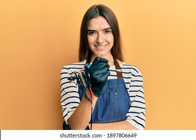 Young Hispanic Woman Tattoo Artist Wearing Professional Uniform And Gloves Smiling With A Happy And Cool Smile On Face. Showing Teeth. 