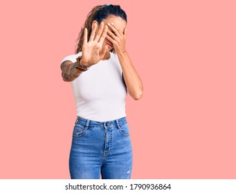 Young Hispanic Woman With Tattoo Wearing Casual White Tshirt Covering Eyes With Hands And Doing Stop Gesture With Sad And Fear Expression. Embarrassed And Negative Concept. 