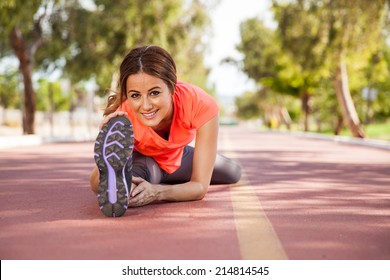 Young Hispanic Woman Touching Her Toes For Stretching At A Running Track