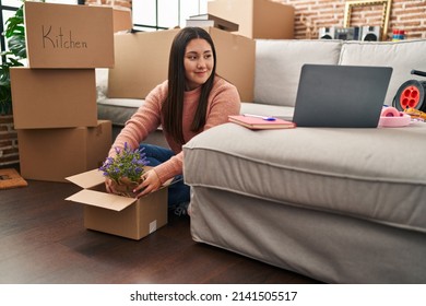 Young Hispanic Woman Unpacking Lavander Plant Of Cardboard Box At New Home