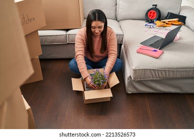 Young Hispanic Woman Unpacking Lavander Plant Of Cardboard Box At New Home