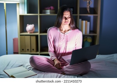 Young Hispanic Woman Using Computer Laptop On The Bed Skeptic And Nervous, Frowning Upset Because Of Problem. Negative Person. 