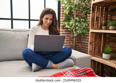 Young Hispanic Woman Using Laptop Sitting On Sofa At Home