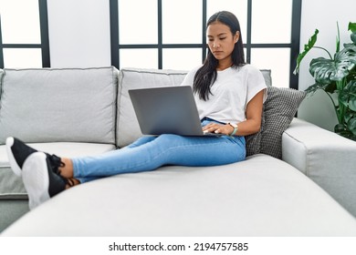 Young Hispanic Woman Using Laptop At Home Sitting On The Sofa Thinking Attitude And Sober Expression Looking Self Confident 