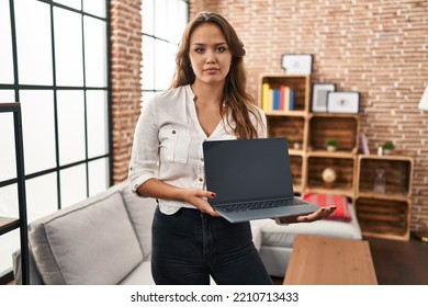 Young Hispanic Woman Using Laptop Showing Blank Screen At Home Thinking Attitude And Sober Expression Looking Self Confident 