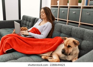 Young hispanic woman using laptop sitting on sofa with dogs at home - Powered by Shutterstock