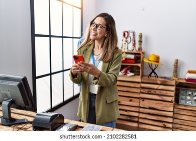 Young hispanic woman using smartphone working at clothing store