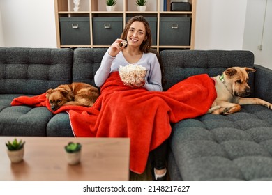 Young hispanic woman watching movie sitting on sofa with dogs at home - Powered by Shutterstock