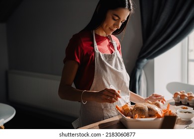 Young Hispanic Woman Wearing Apron Cooking Chicken In Kitchen At Home