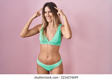 Young Hispanic Woman Wearing Bikini Over Pink Background Smiling Pointing To Head With Both Hands Finger, Great Idea Or Thought, Good Memory 