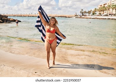 Young hispanic woman wearing bikini holding towel at seaside