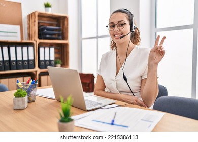 Young Hispanic Woman Wearing Call Center Agent Headset At The Office Smiling With Happy Face Winking At The Camera Doing Victory Sign. Number Two. 