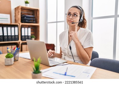 Young Hispanic Woman Wearing Call Center Agent Headset At The Office Serious Face Thinking About Question With Hand On Chin, Thoughtful About Confusing Idea 