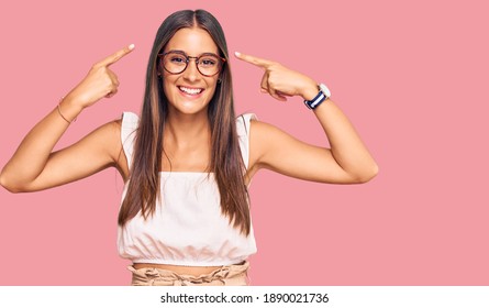 Young Hispanic Woman Wearing Casual Clothes And Glasses Smiling Pointing To Head With Both Hands Finger, Great Idea Or Thought, Good Memory 