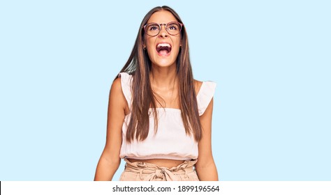 Young hispanic woman wearing casual clothes and glasses angry and mad screaming frustrated and furious, shouting with anger. rage and aggressive concept. 